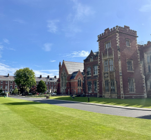 Historisches Geb&auml;ude der Queen&rsquo;s University Belfast mit gepflegtem Rasen unter blauem Himmel.