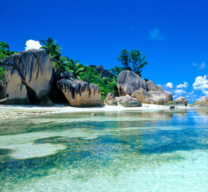 Traumstrand auf den Seychellen mit markanten Granitfelsen, kristallklarem Wasser und &uuml;ppiger tropischer Vegetation unter strahlend blauem Himmel.
