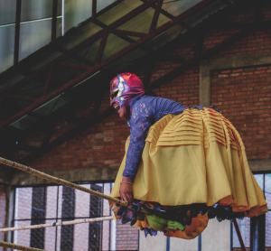 Aymara-Frau in bunter Tracht und Wrestling-Maske steht auf den Ringseilen in einer Halle in La Paz.