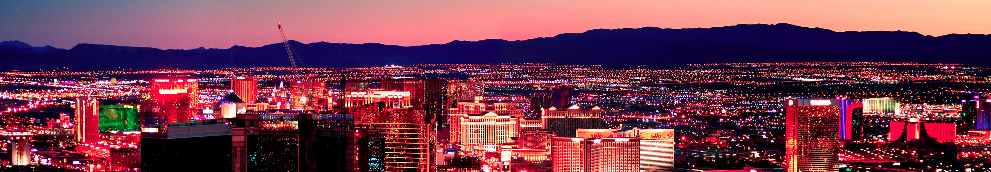 Blick auf den Las Vegas Strip bei Sonnenuntergang, die bunten Neonlichter der Hotels und Casinos erleuchten die Skyline vor der Kulisse der Berge.