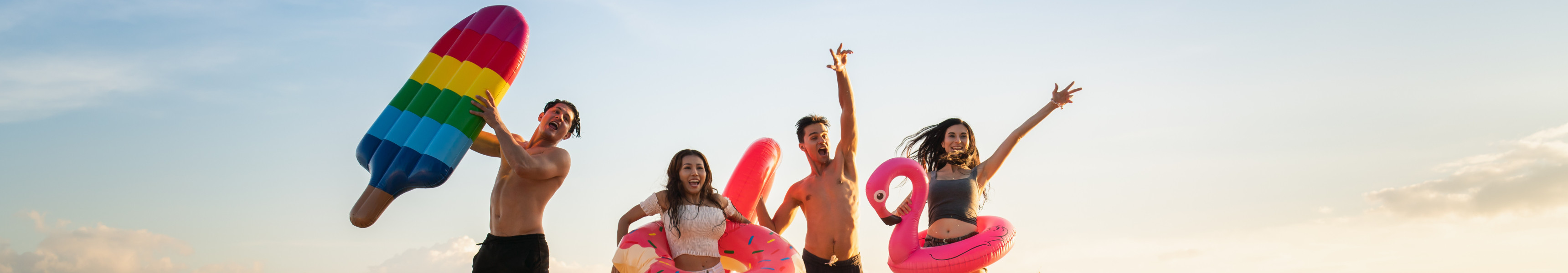Familie mit Luftmatratzen springen am Strand in die H&ouml;he