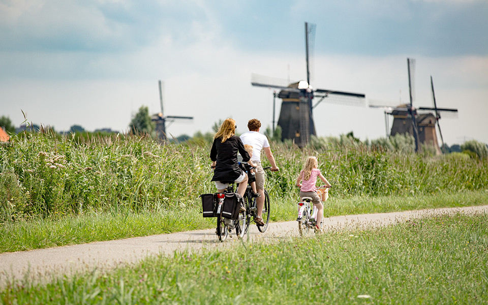 Familie f&auml;hrt Rad zwischen Windm&uuml;hlen und Wiese