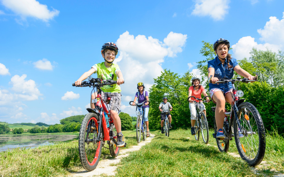 Familie und Kinder fahren mit dem Fahrrad entlang eines Weges am Gardasee bei schönem Wetter.