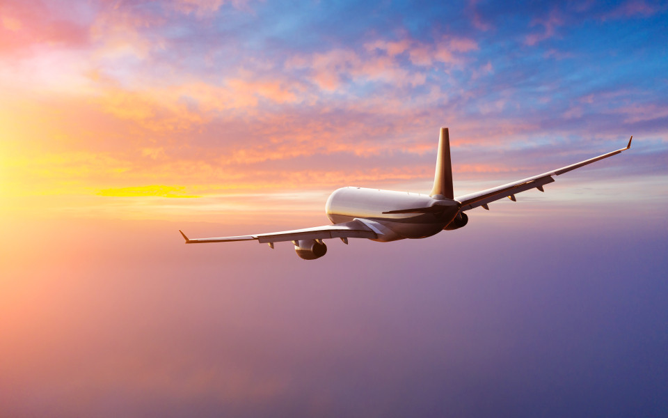 Ein Passagierflugzeug fliegt in den Sonnenuntergang, was eine typische Herausforderung f&uuml;r den Jetlag bei Reisen von West nach Ost darstellt.