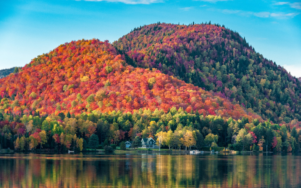 Die mit roten Ahornw&auml;ldern bedeckten H&uuml;gel hinter einem Holzhaus am Ufer eines Sees in Quebec, an einem wundersch&ouml;nen Herbstabend.