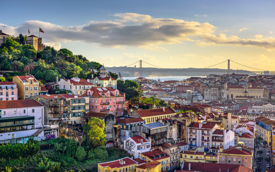 Blick auf das Stadtbild von Lissabon, mit dem Castelo de São Jorge im Hintergrund und der 25 de Abril Brücke über dem Tejo-Fluss.