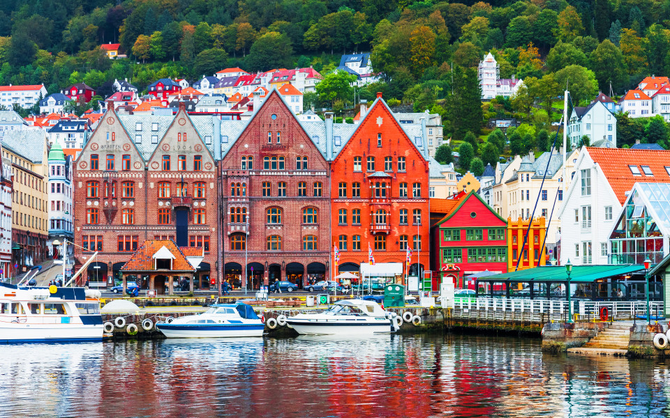 Bunte Häuser am Hafen von Bergen mit Booten im Vordergrund und grünen Hügeln im Hintergrund.