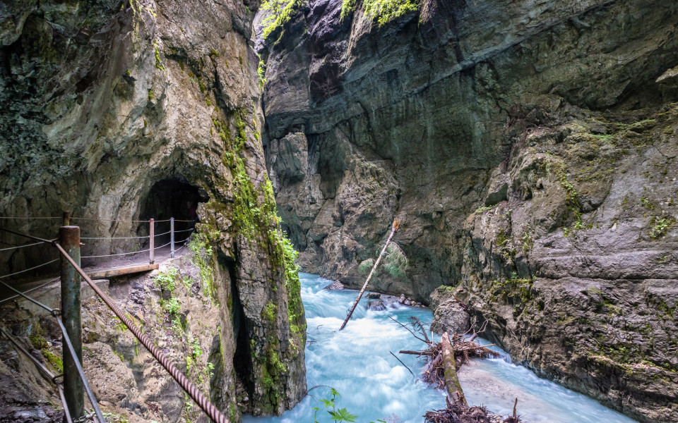 Schmale Schlucht mit t&uuml;rkisblauem Wildbach, steilen Felsw&auml;nden und einem in den Fels gehauenen Wanderweg mit Gel&auml;nder in der Partnachklamm bei Garmisch-Partenkirchen, Bayern. 